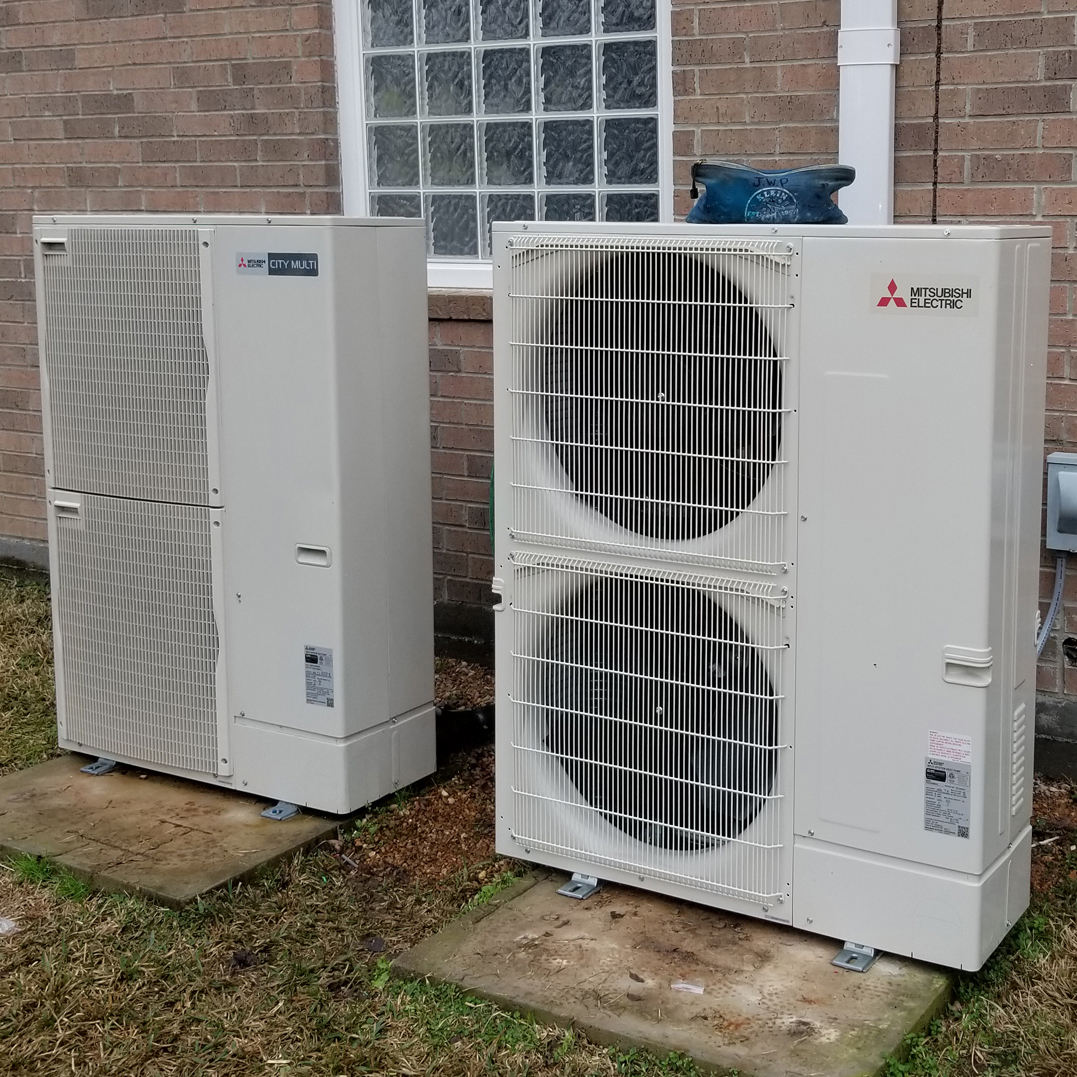 Two air conditioners are outside on the ground.